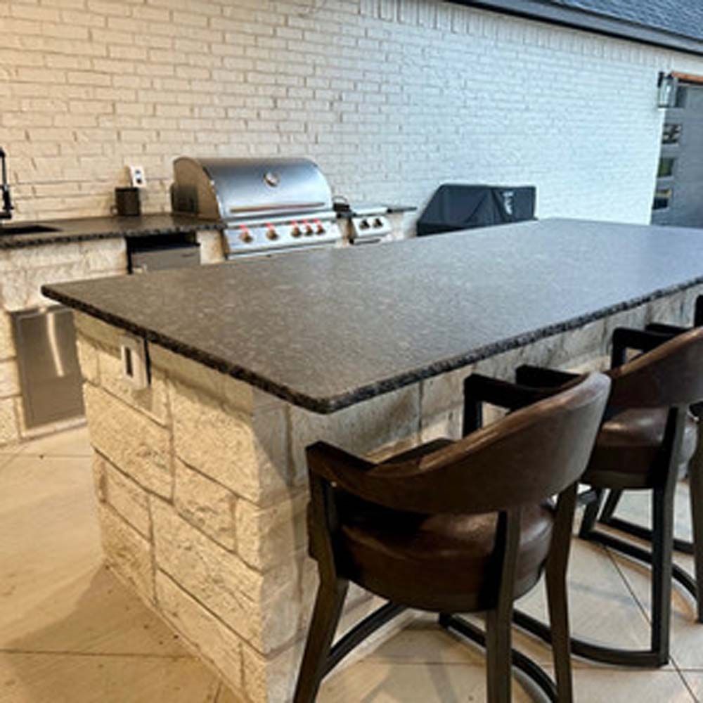 Outdoor kitchen with a stone-faced island, dark countertop, stainless steel grill, and brown leather bar stools.