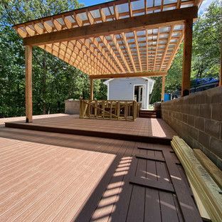 Wooden deck with pergola. Bar area under the structure, with a retaining wall and woods in the background.