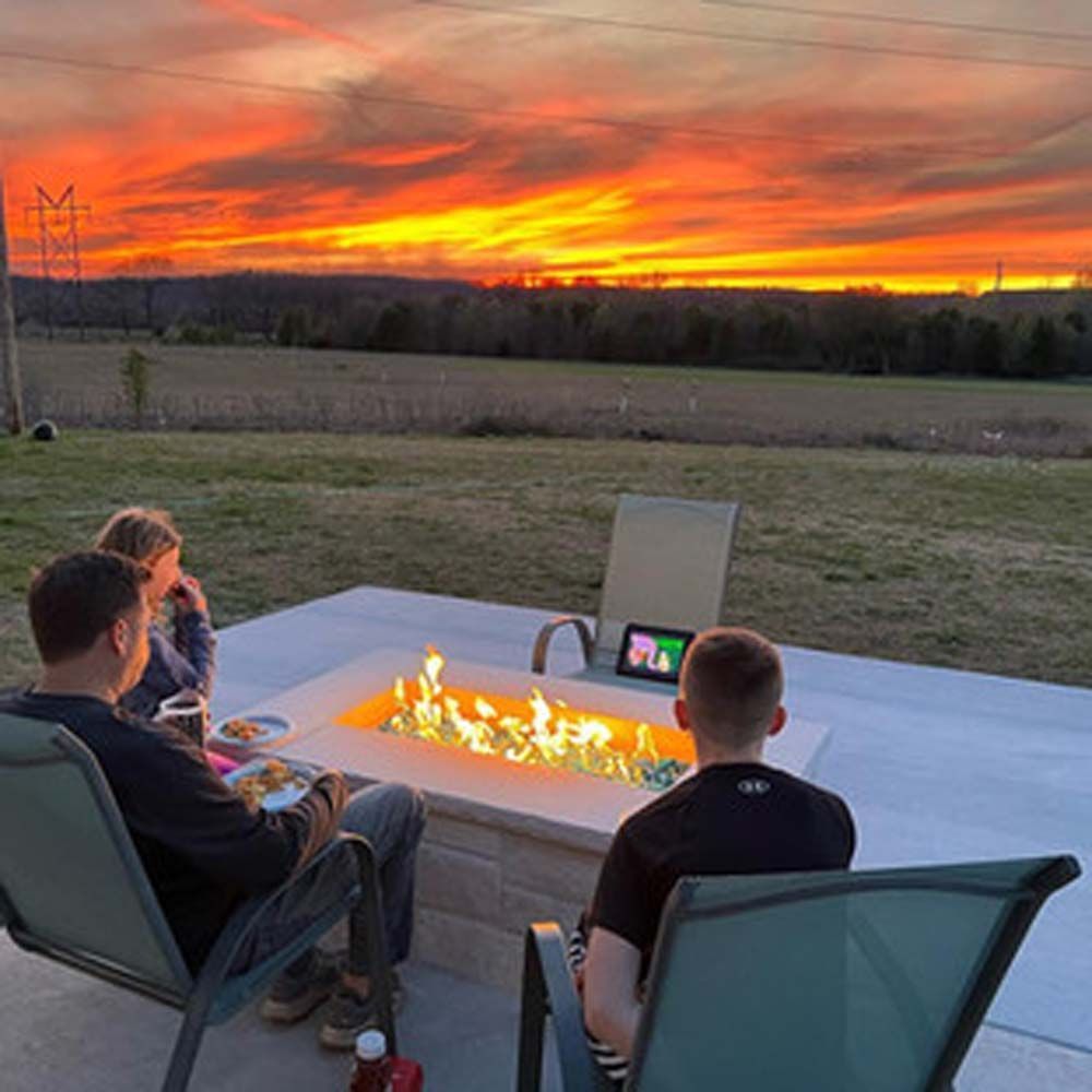 People around a fire pit, watching a sunset. The sky is bright orange and red.