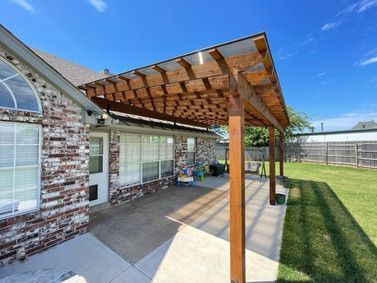 Patio with wooden pergola attached to a brick house; a sunny day.