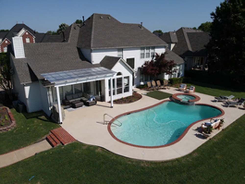 Backyard with a pool, patio, and white house under a bright sunny sky.