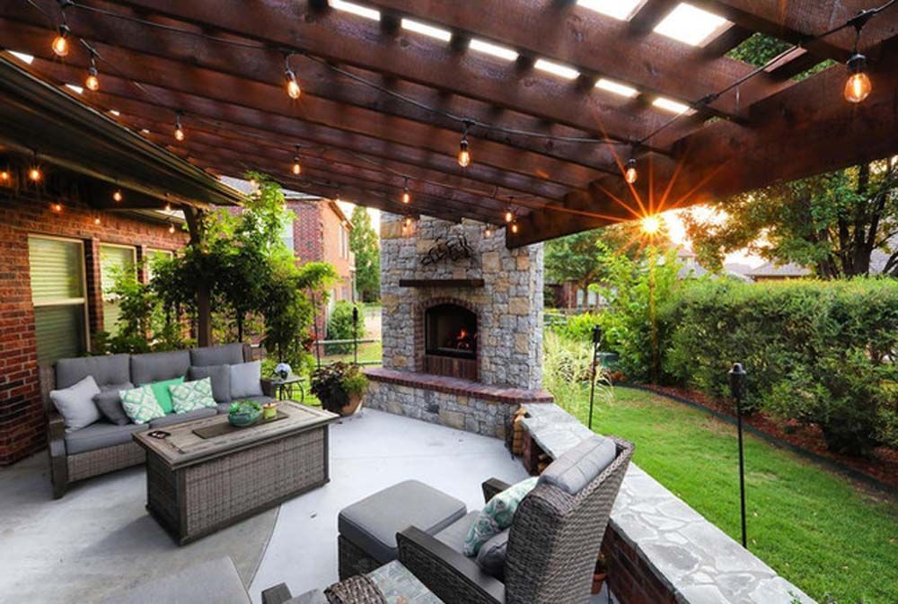 Outdoor patio with fireplace, seating, string lights under a pergola, and sunset view.