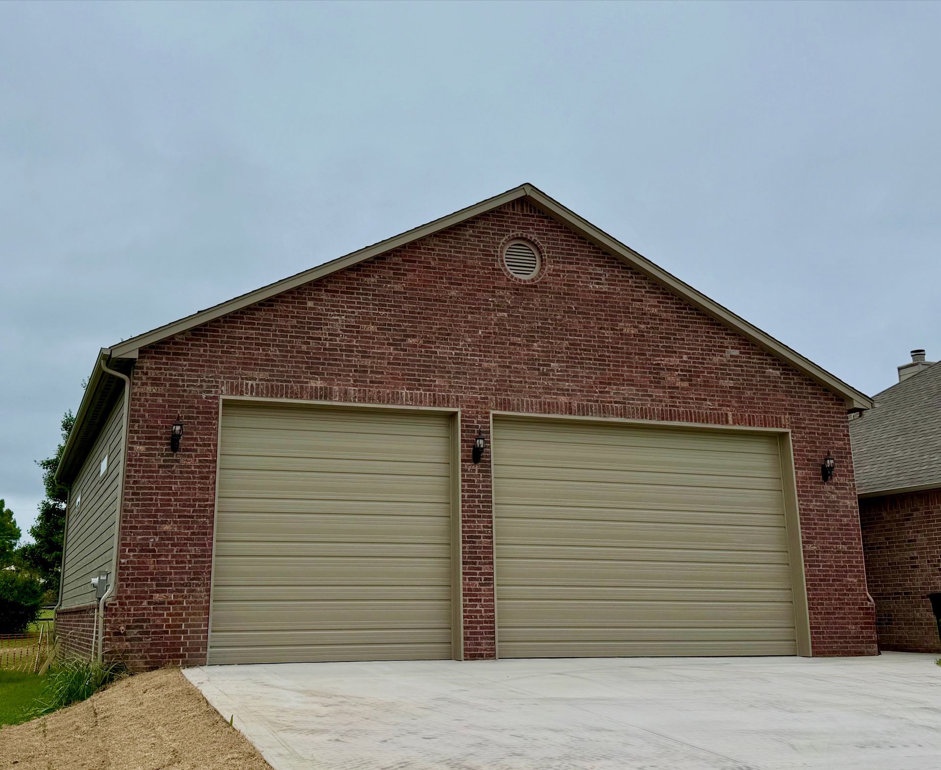 A concrete driveway leading to a gray garage with a white door, adjacent to a brick house.