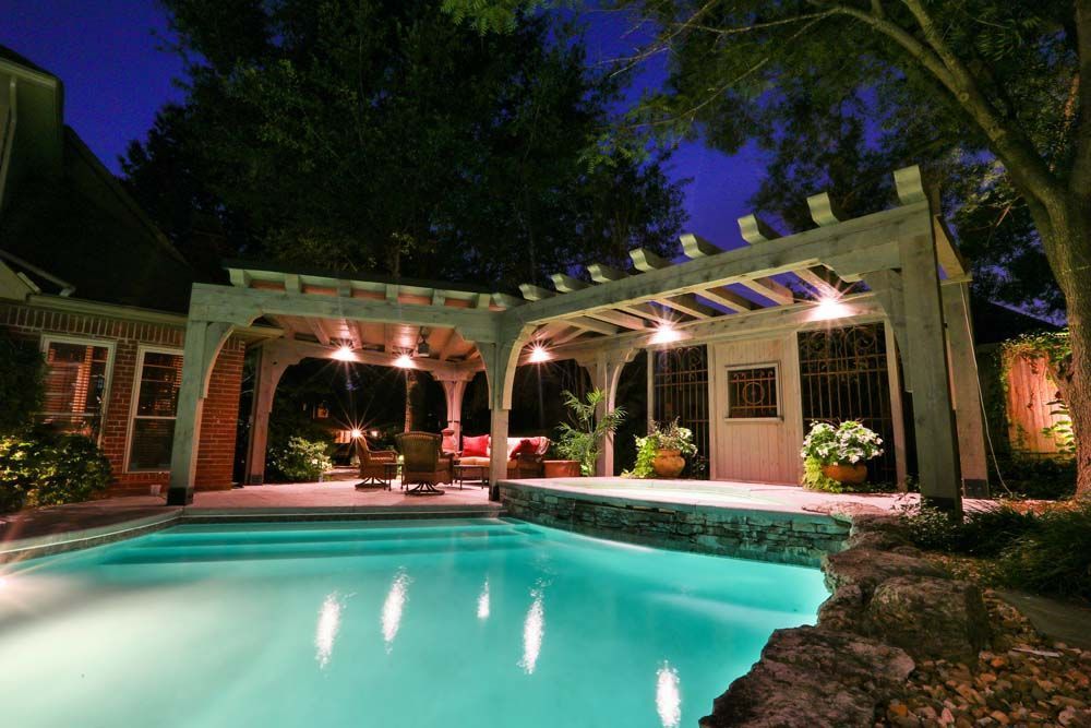 Nighttime view of a lit pool with a pergola and seating area.