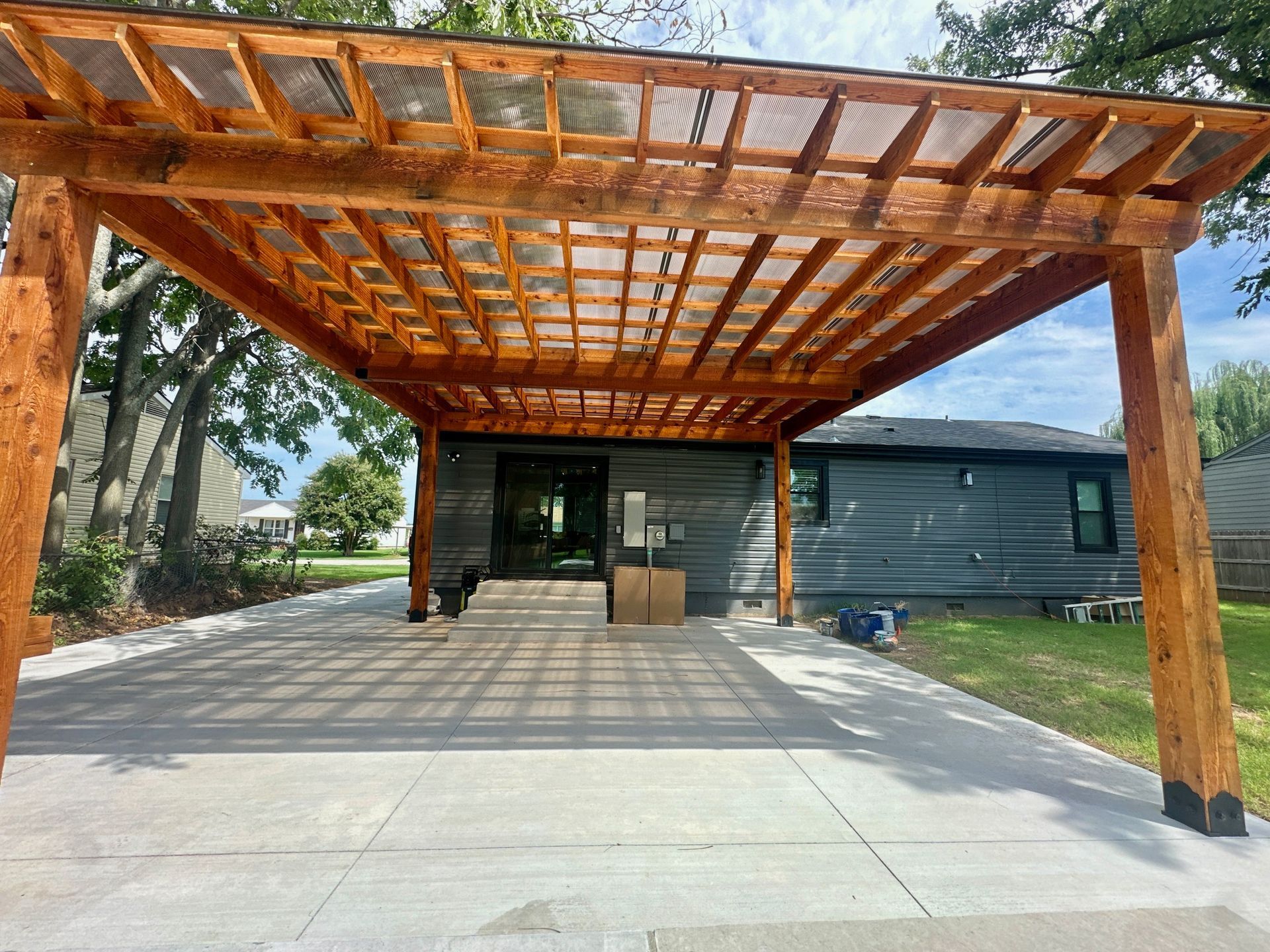 Wooden pergola over a concrete driveway; home in background.