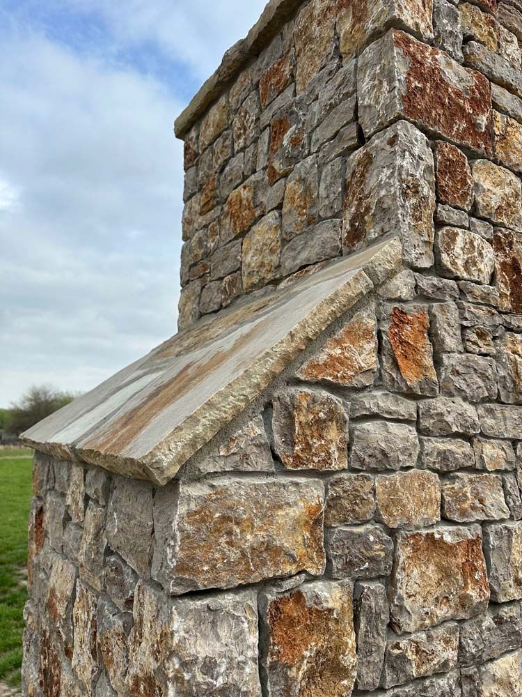 Corner of a stone structure with a gray cap, against a cloudy sky.