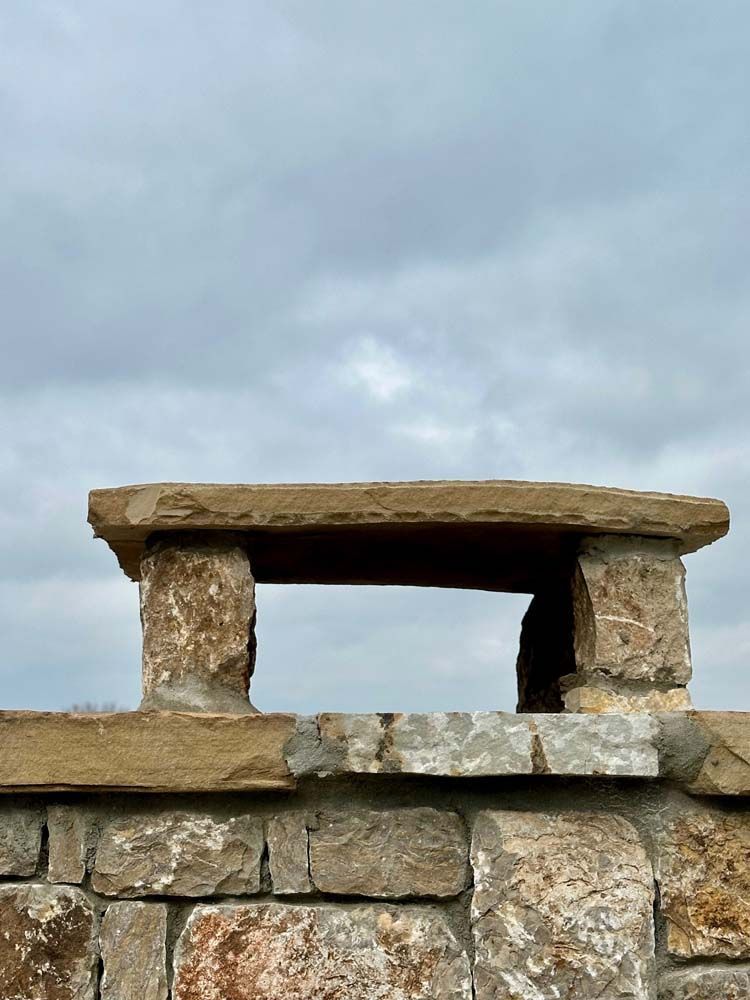 Stone chimney with a rectangular opening against a cloudy sky.