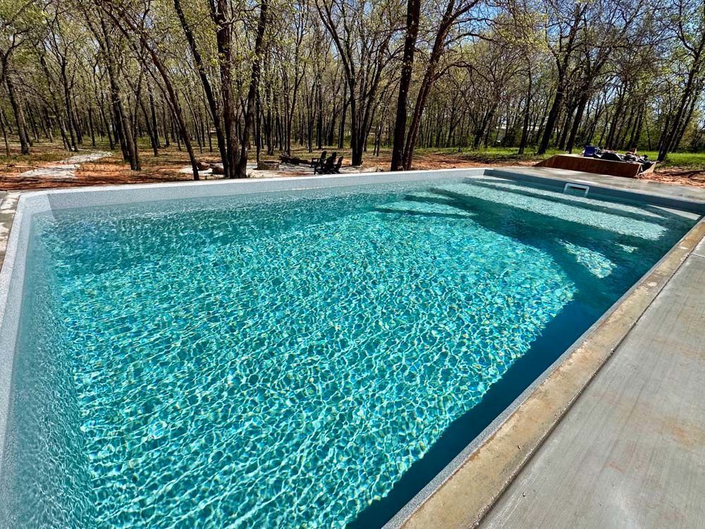A rectangular pool filled with turquoise water, surrounded by concrete, set amidst a forest with bare trees.