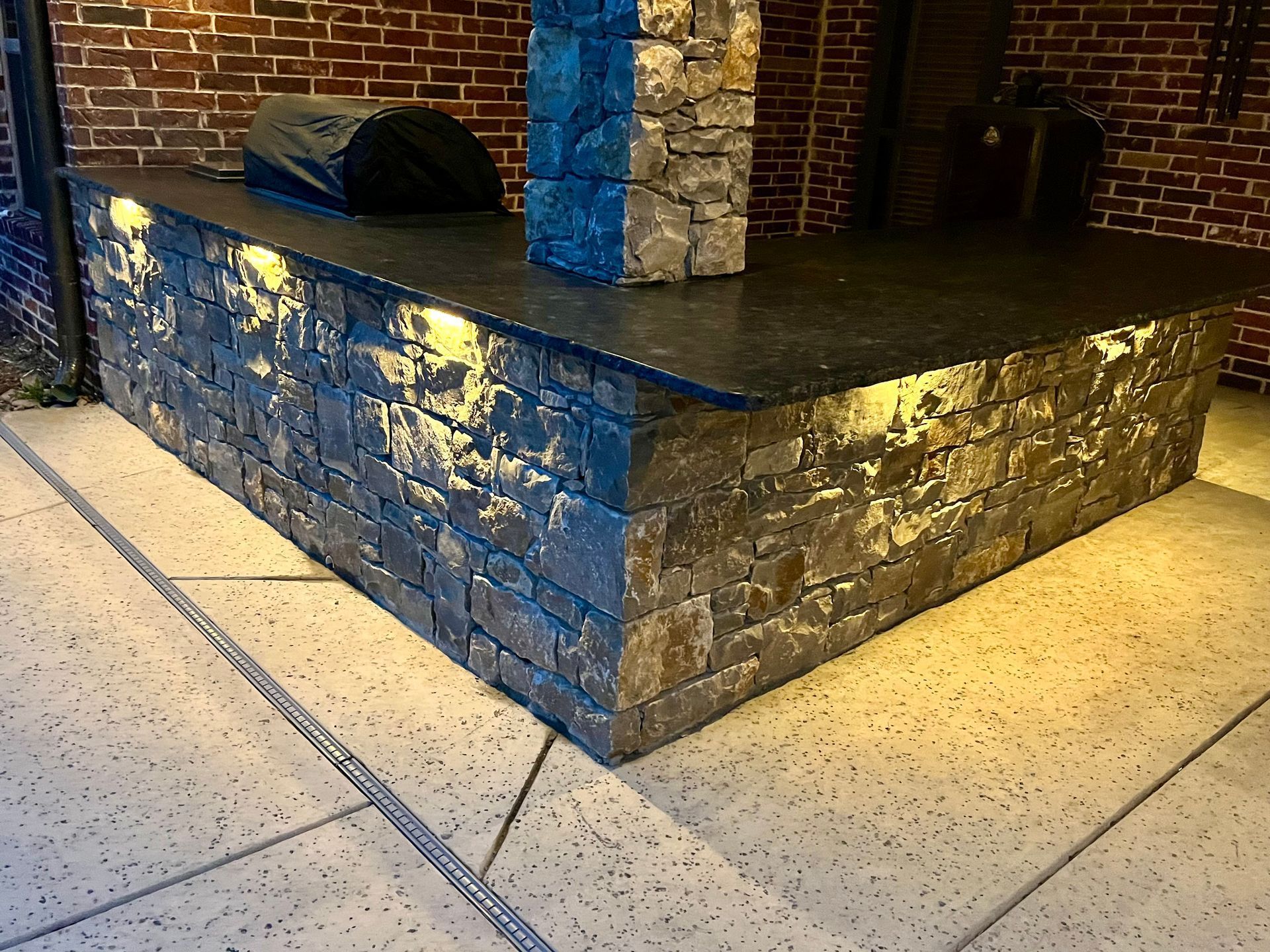 Stone bar with black countertop and built-in lighting, set against a brick wall.