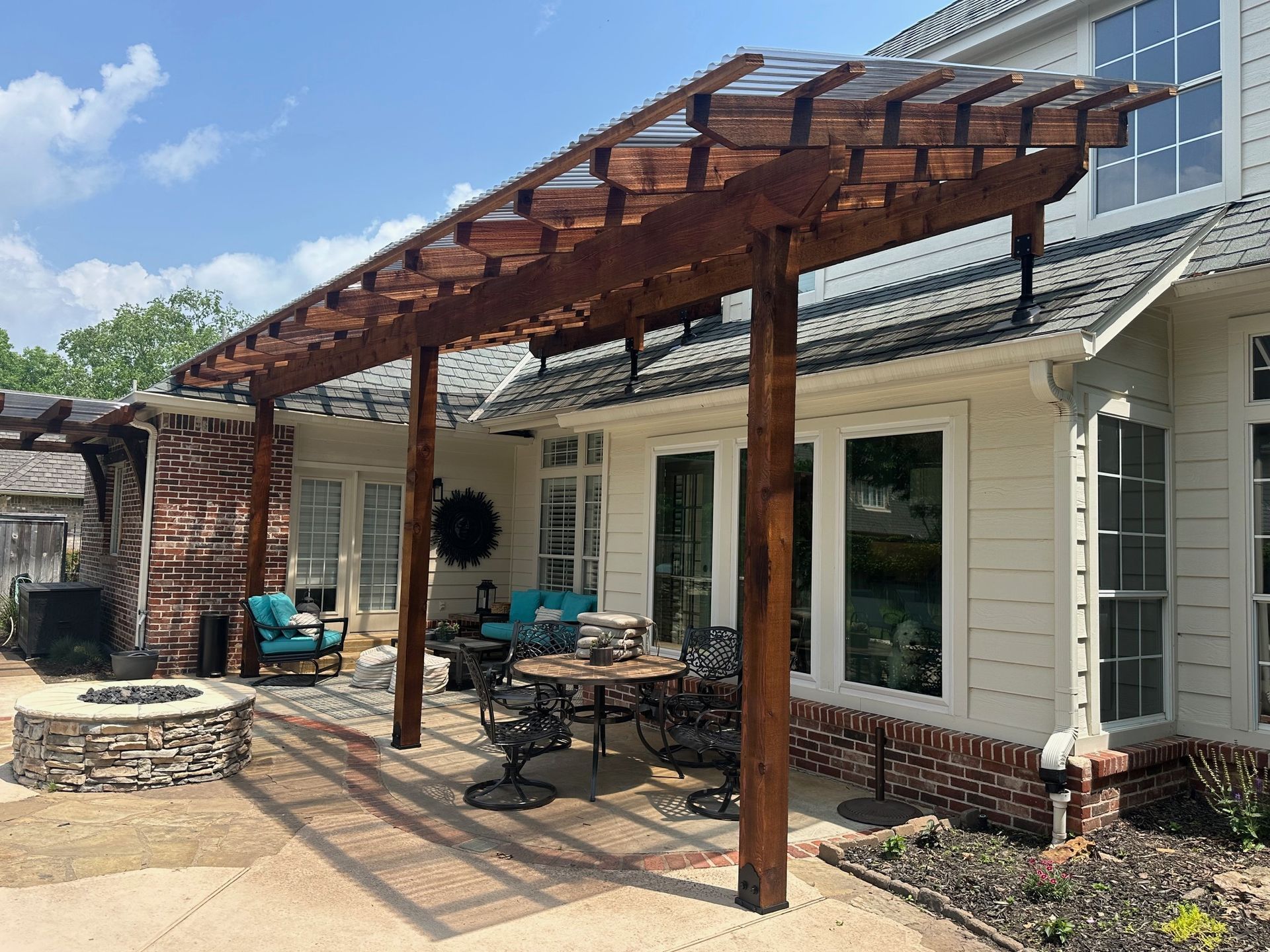 Wooden pergola attached to a white house with outdoor seating and fire pit.