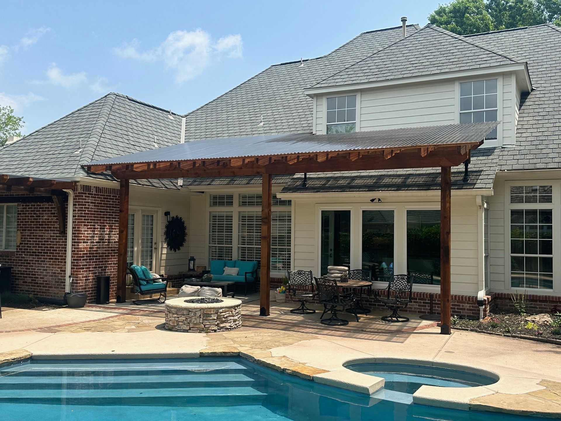 Poolside patio with pergola attached to a two-story white house; a pool and fire pit are in view.
