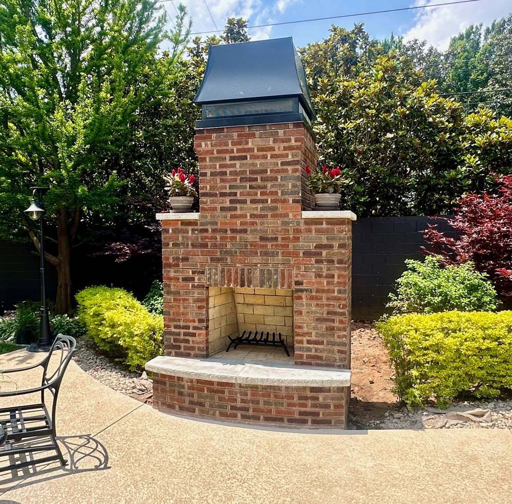 Brick outdoor fireplace with black chimney cap, surrounded by landscaping.