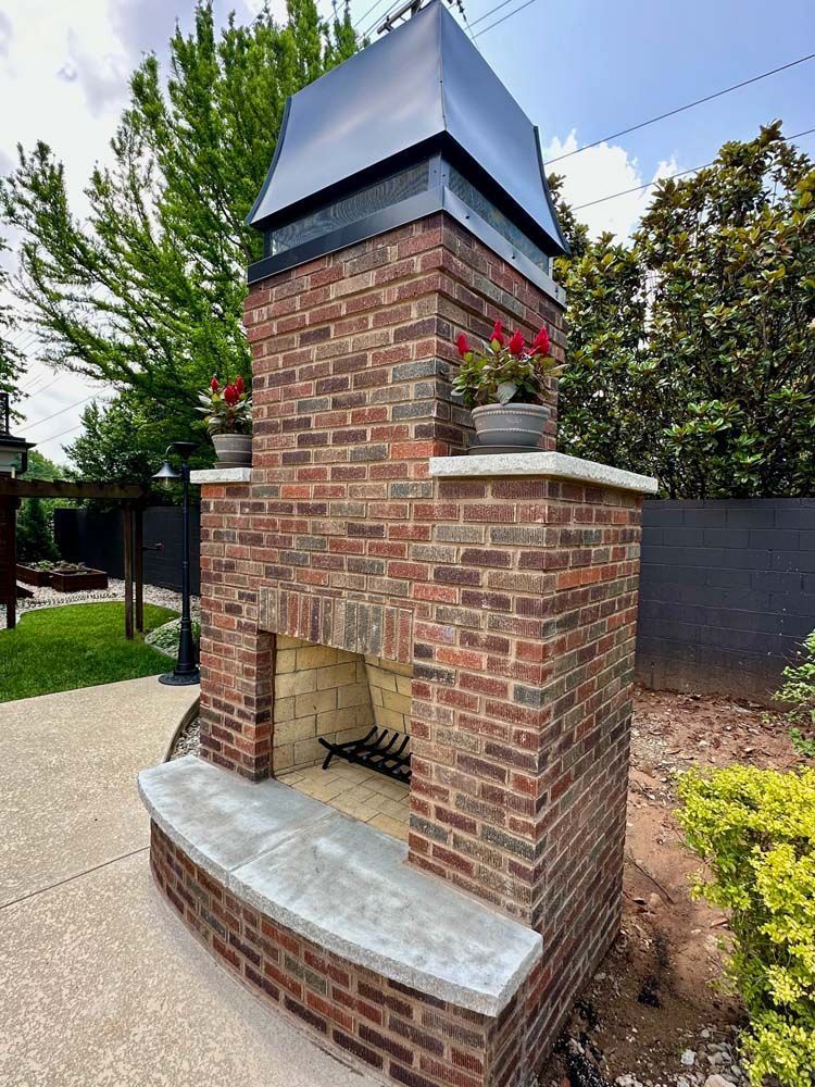 Brick outdoor fireplace with a black top and red flowers on top; on a patio.