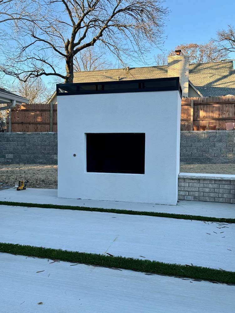 White outdoor structure with a black rectangle; set in a backyard with trees and fence.
