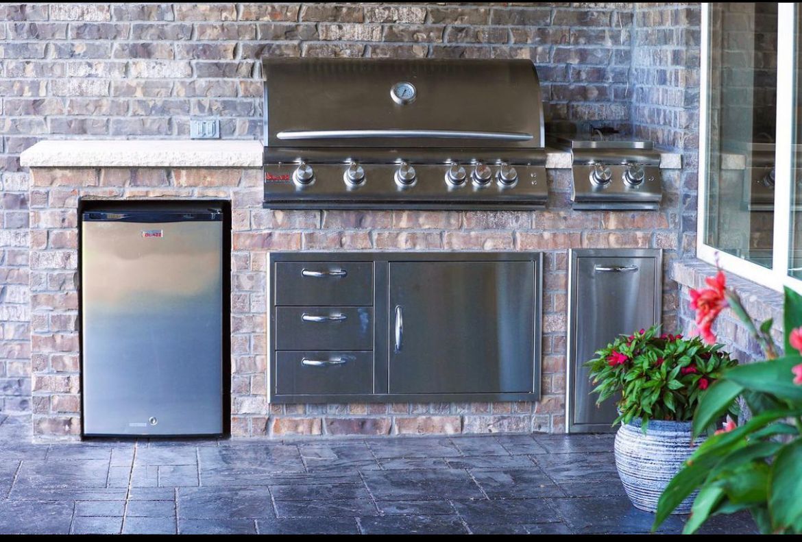 Outdoor kitchen with grill, refrigerator, storage, and brick wall.
