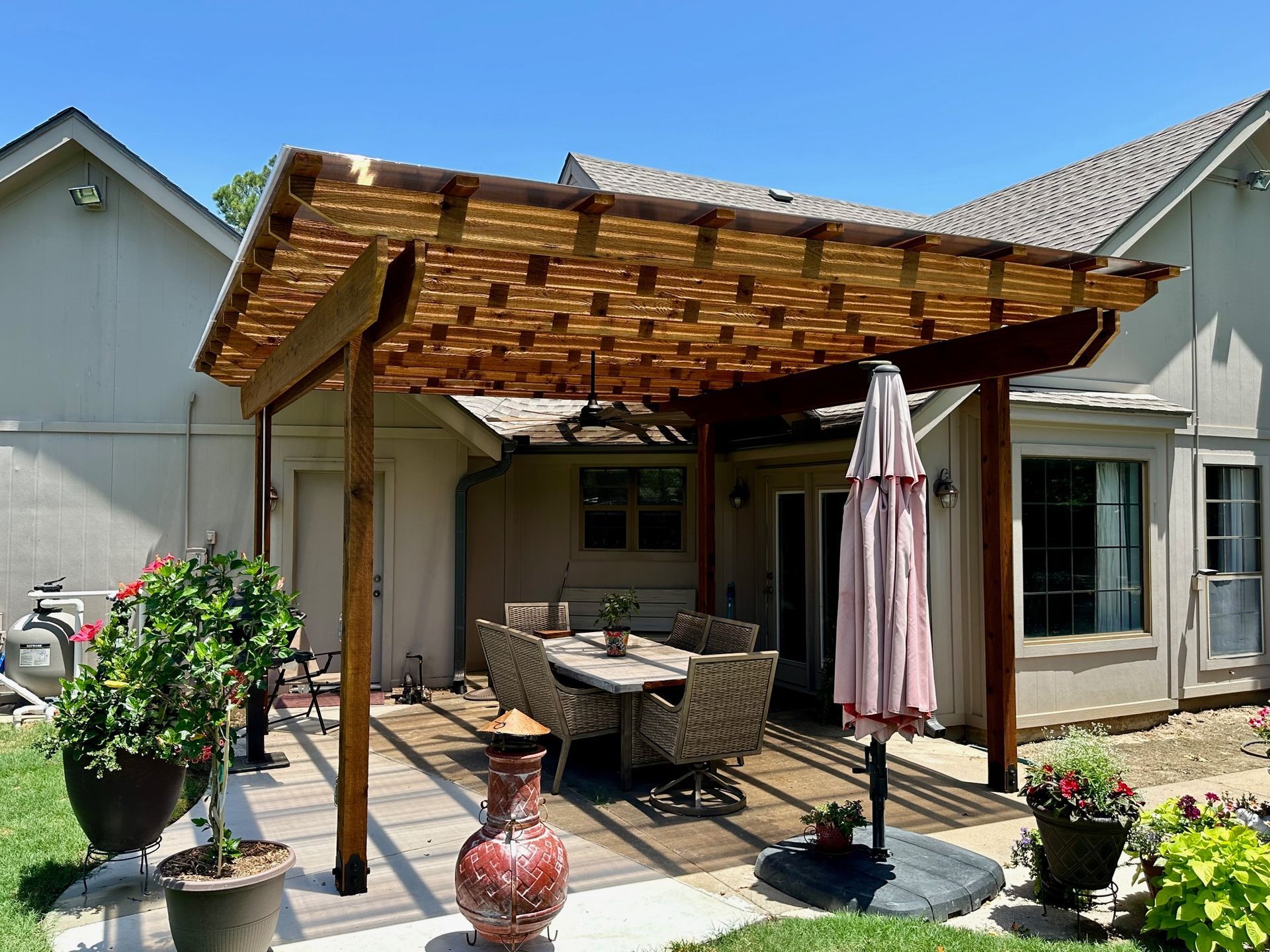 Pergola with woven roof over patio furniture, beside a house.