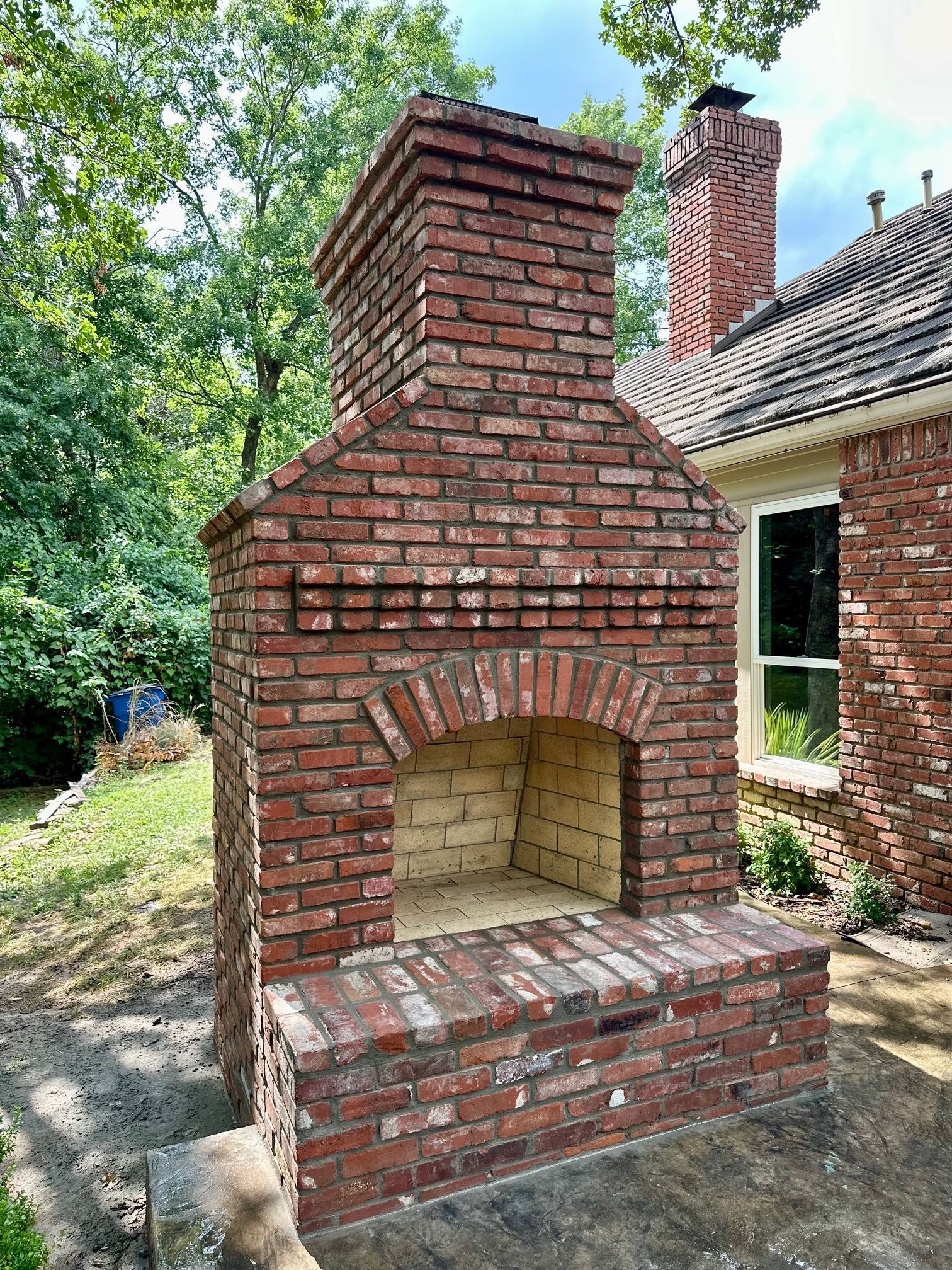 Brick outdoor fireplace with chimney, red brick, stone patio, backyard setting.