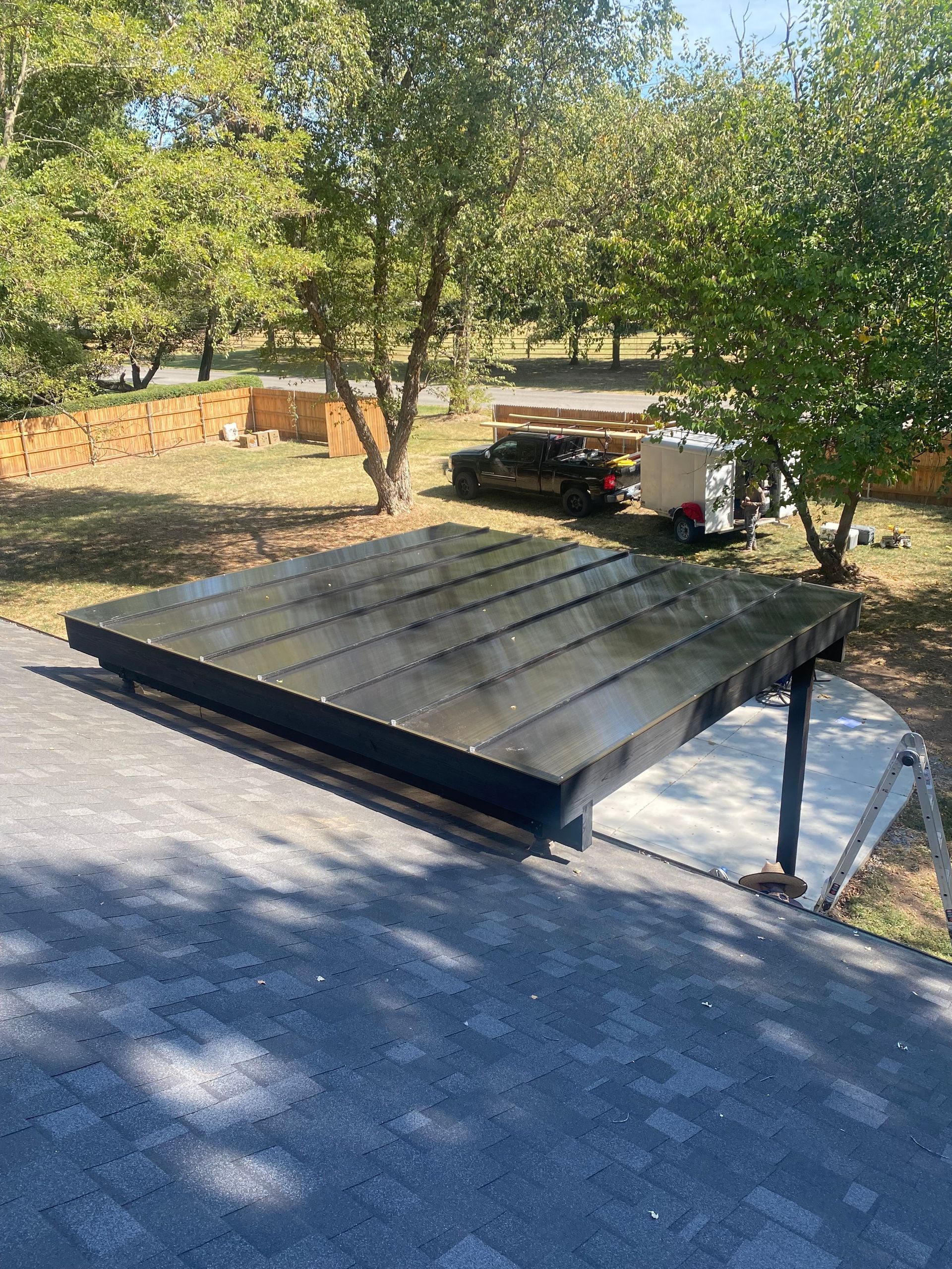 Black solar panels installed on a roof, with trees and equipment in the background on a sunny day.