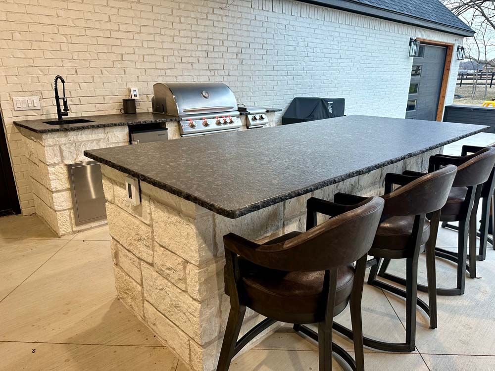 Outdoor kitchen with a brick island, grill, sink, countertop, and bar stools.