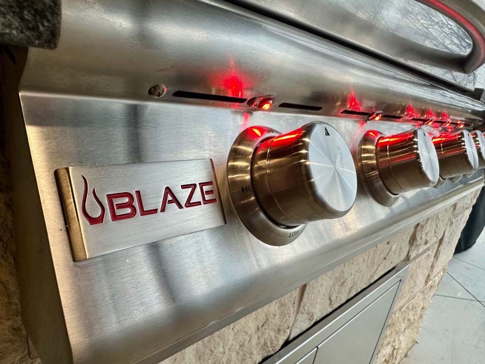 Close-up of a stainless steel Blaze grill with illuminated red control knobs and logo.