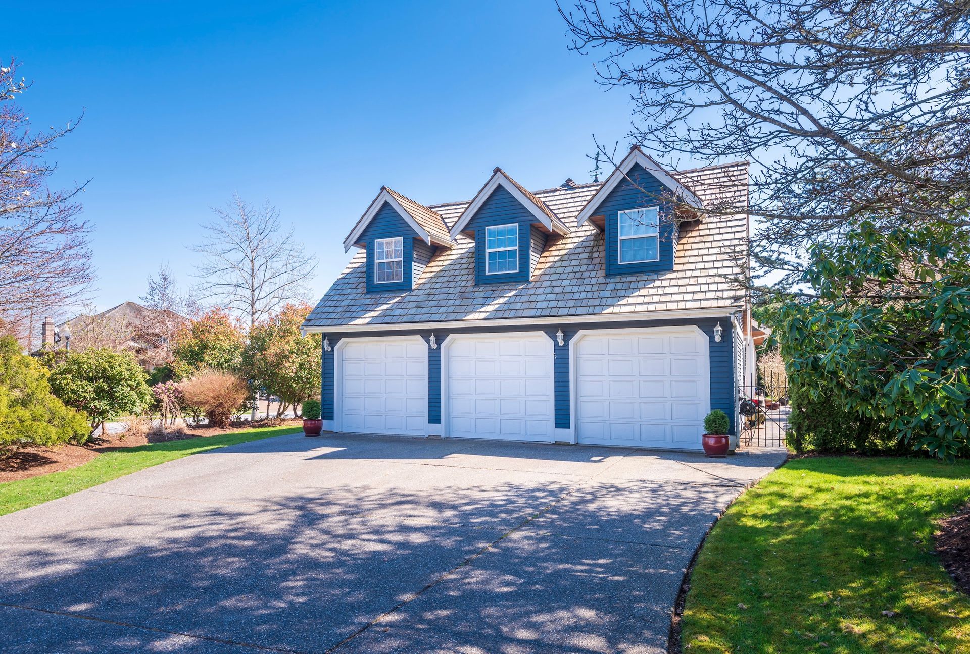 Three-car garage with blue trim and three dormers, on a driveway with lawn and trees.