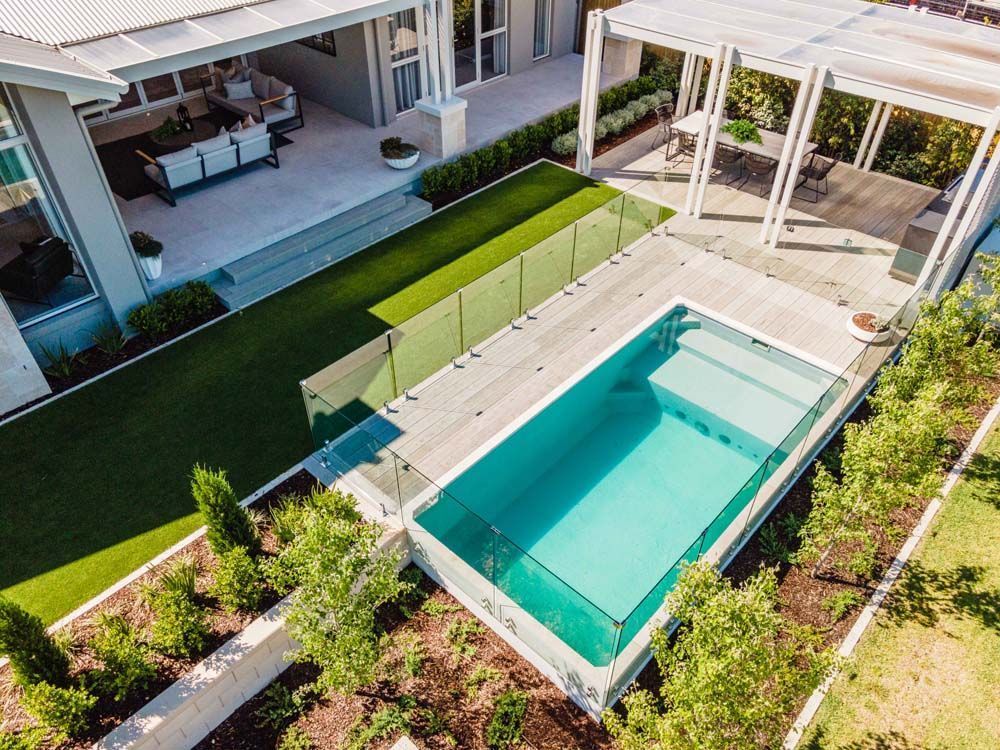 Aerial view of a modern home with a pool, patio, and lawn. White, beige, and green colors are prevalent.