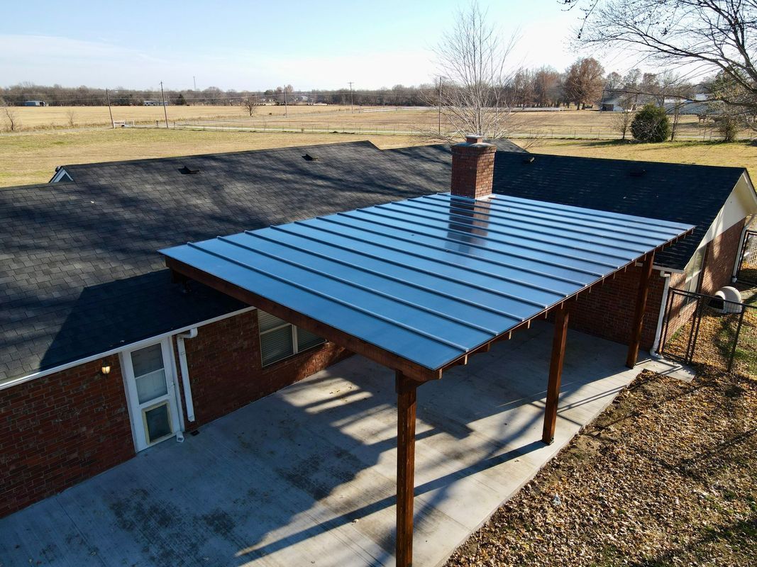 Carport with metal roof attached to a brick house. Sunny, rural setting.