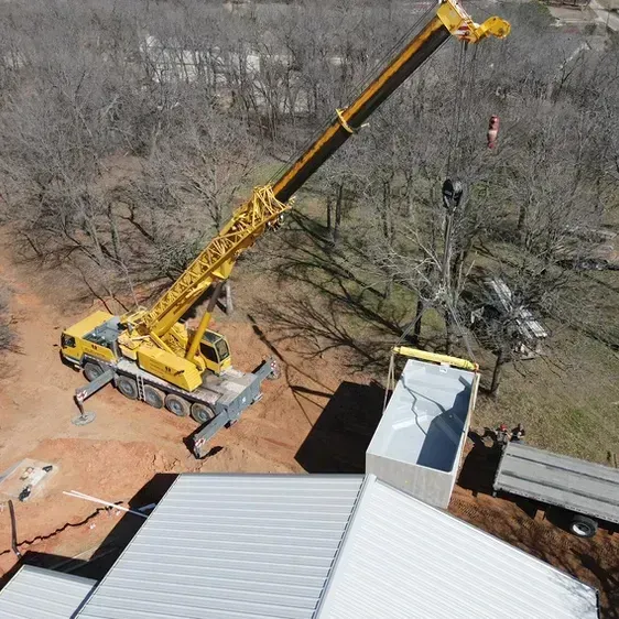 A yellow crane lifts a container onto a roof near trees.