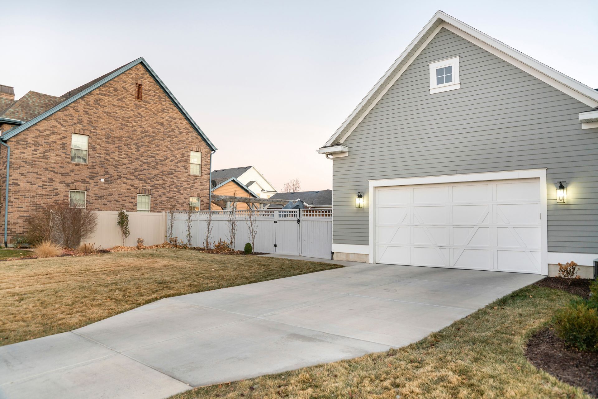 A concrete driveway leading to a gray garage with a white door, adjacent to a brick house.