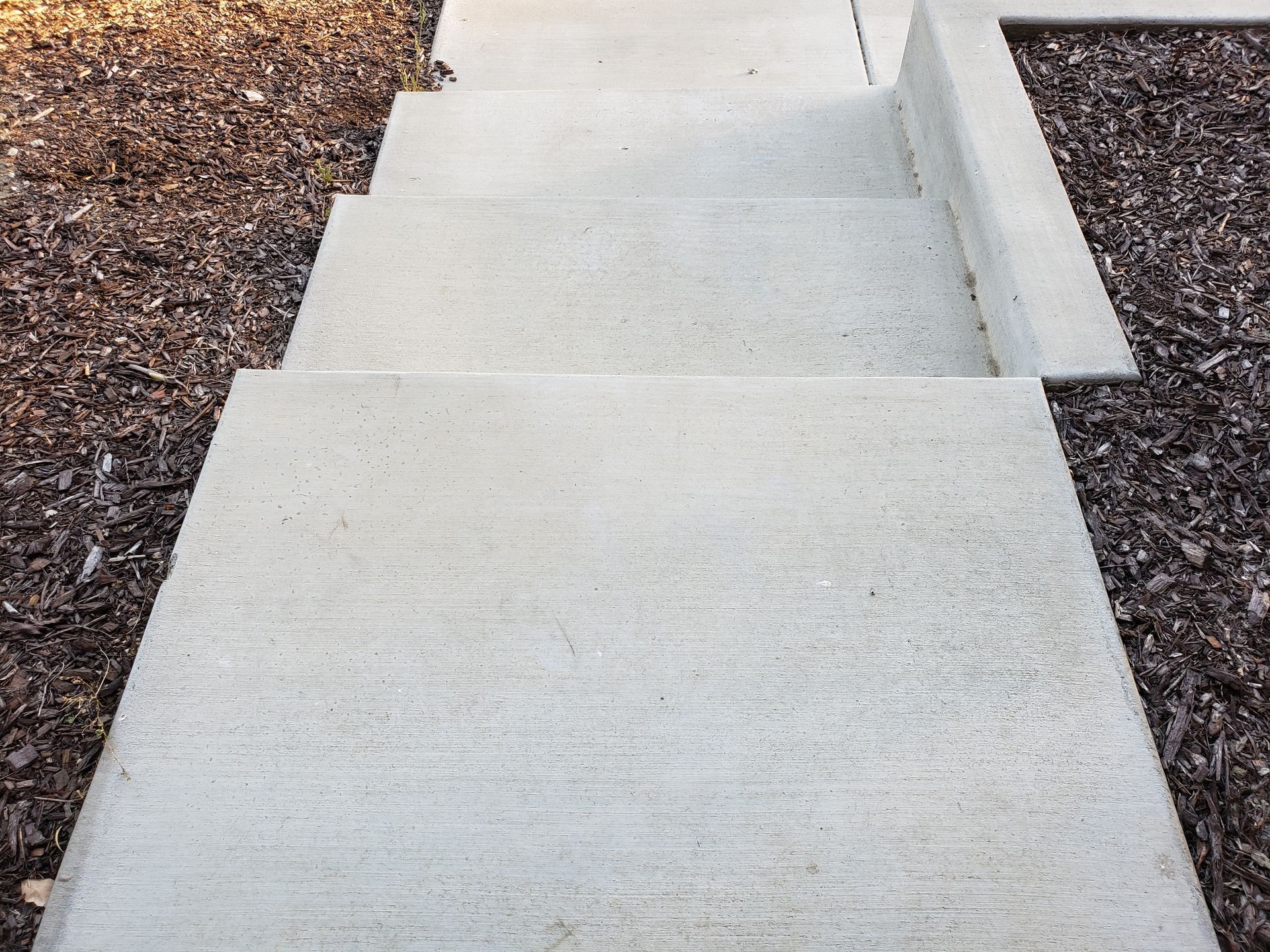 Concrete steps leading down, surrounded by brown mulch.
