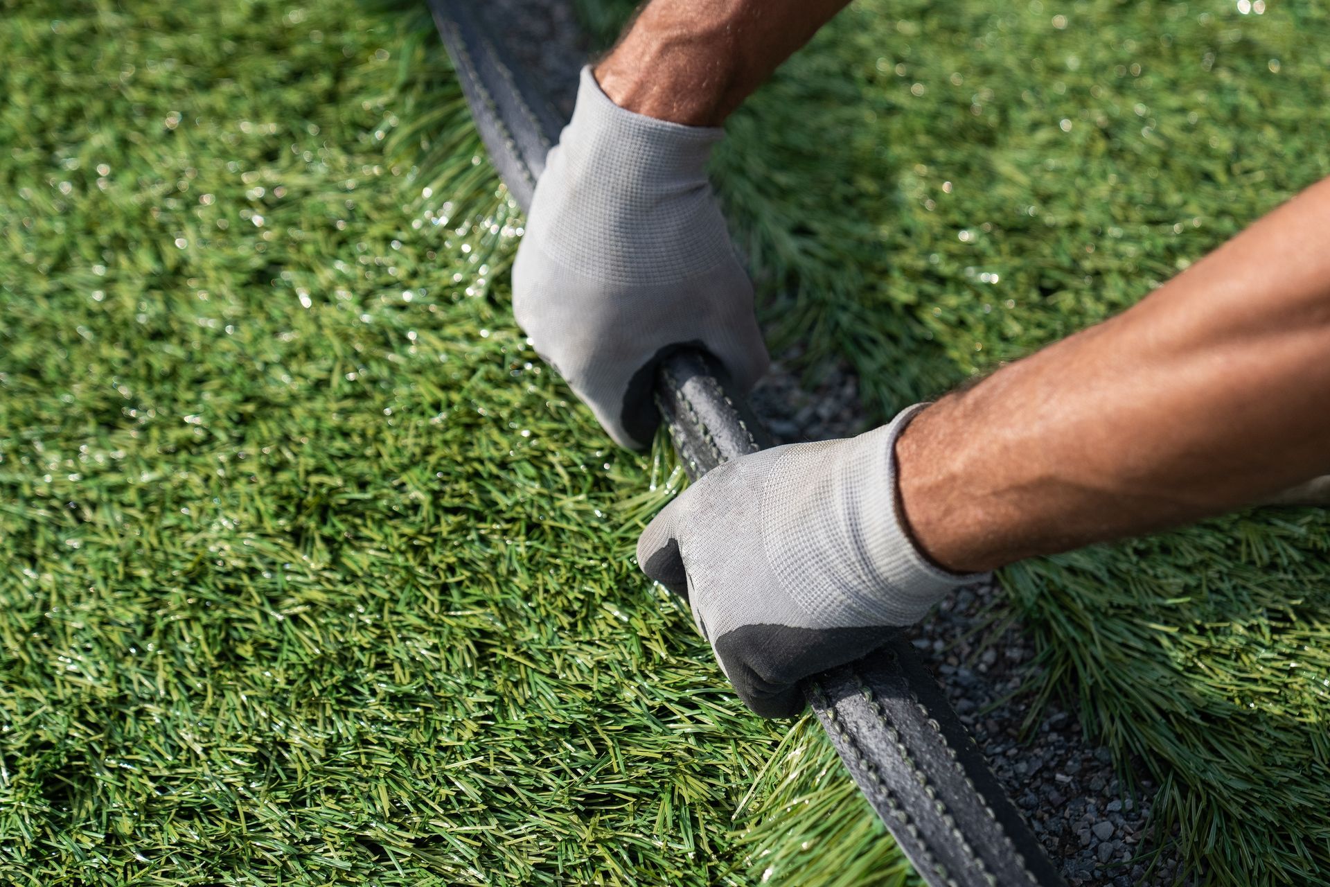 Hands wearing gloves joining two pieces of artificial turf.