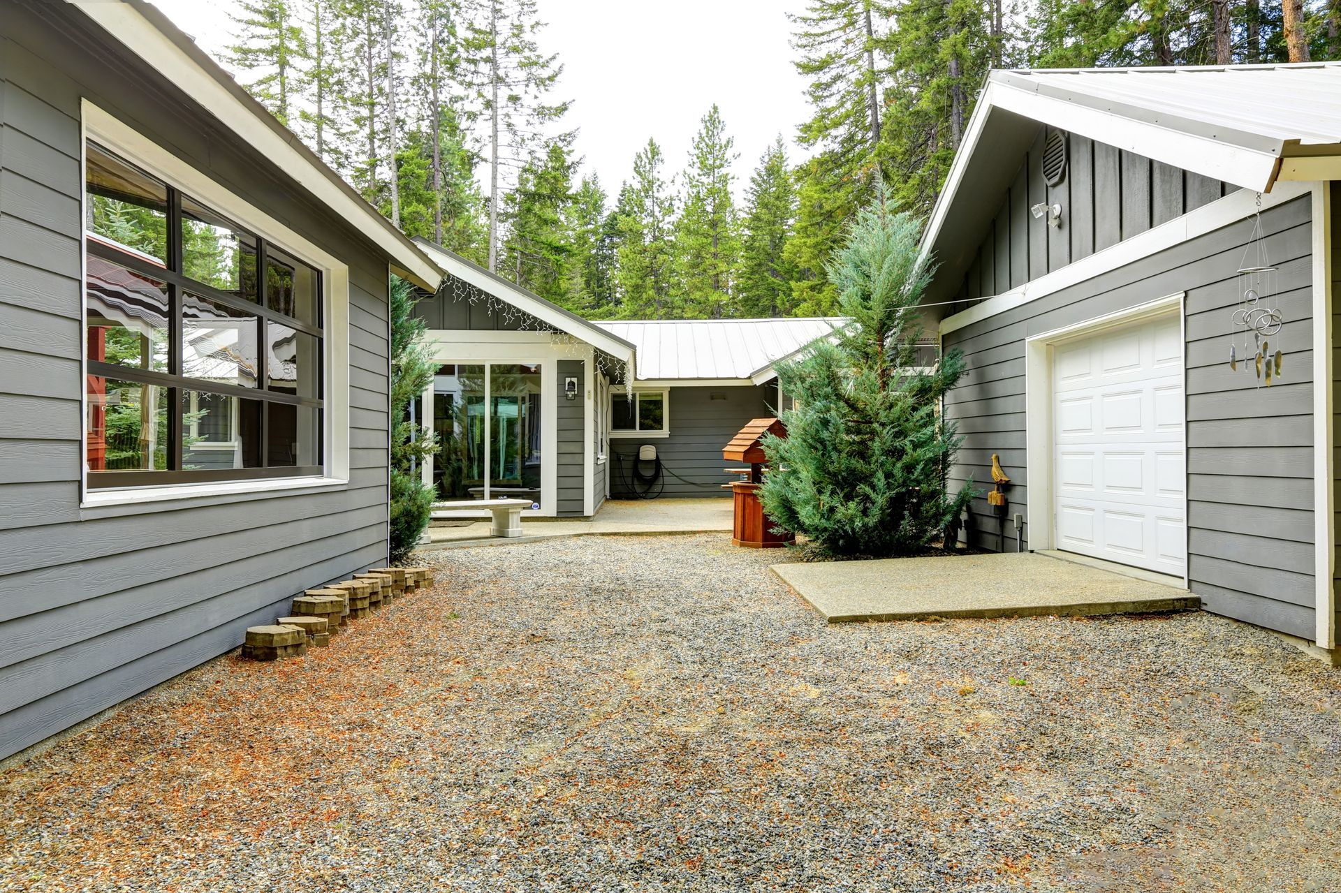Gray house with gravel yard, surrounded by trees.