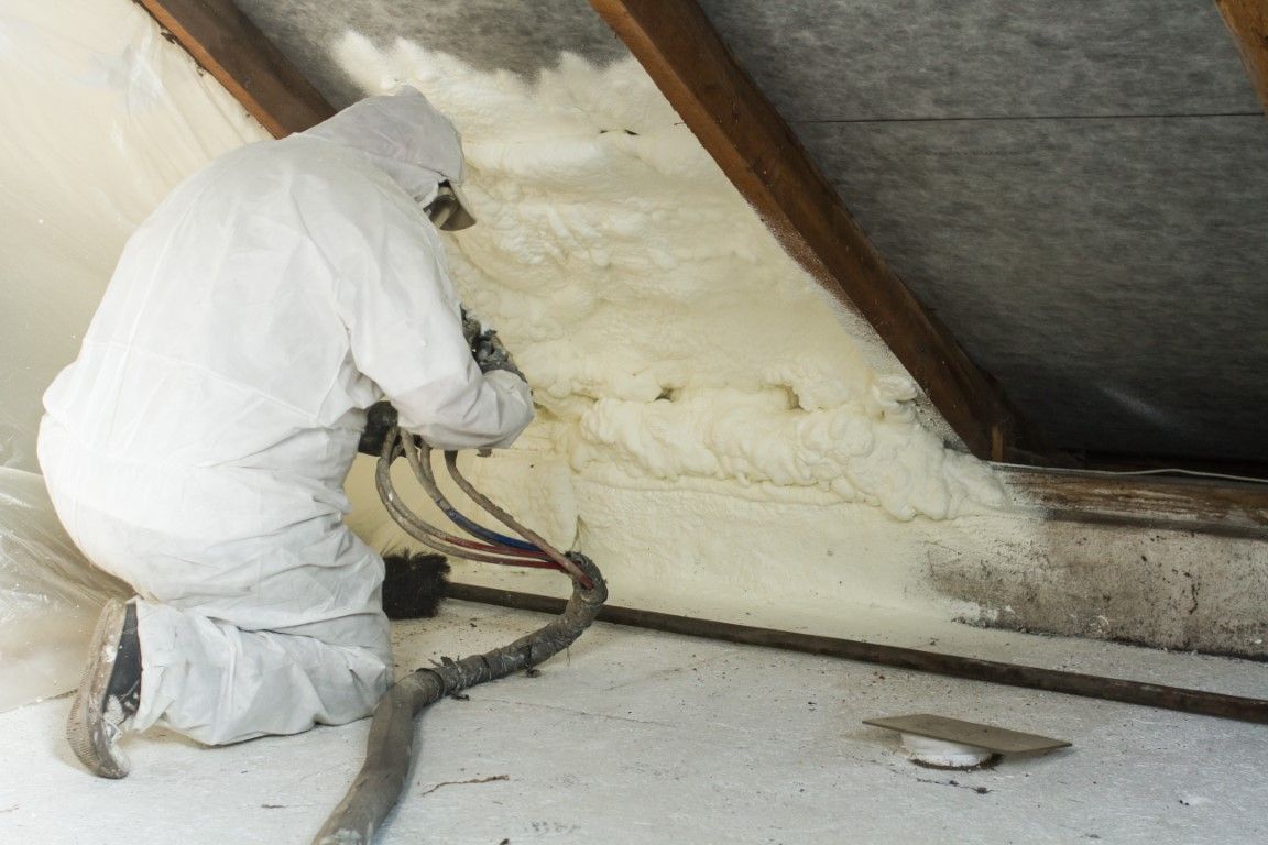 Worker in white protective suit spraying foam insulation into an attic wall