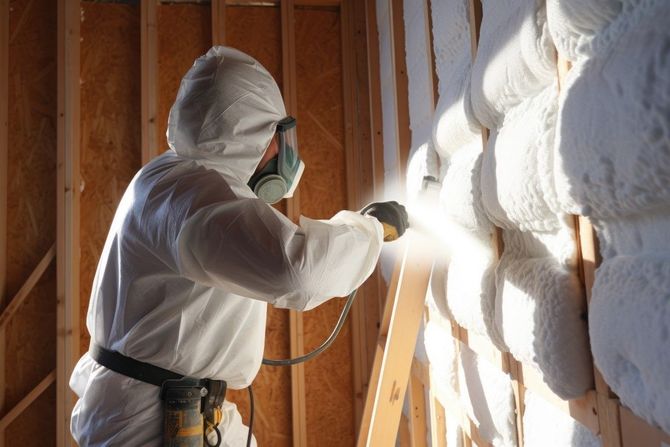 Worker spraying foam insulation inside a wooden wall frame