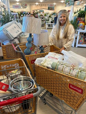 A person smiles while pushing a shopping cart filled with home decor items in a retail store.