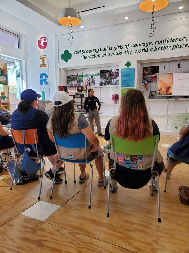 A speaker stands before a group of people sitting on chairs in a Girl Scouts facility.