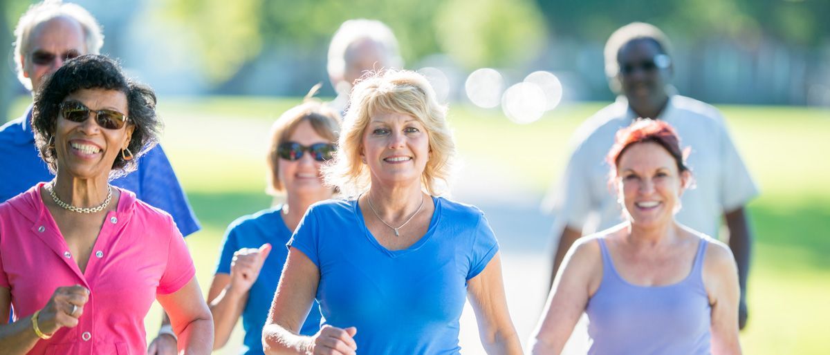 A group of people wearing casual exercise clothing jogging together on a sunny, blurred outdoor path.