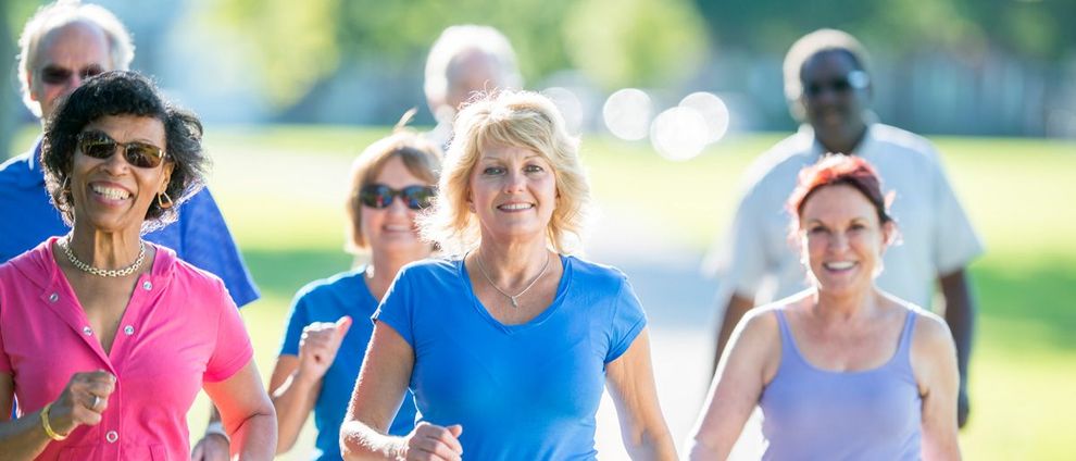 A group of people wearing casual exercise clothing jogging together on a sunny, blurred outdoor path.