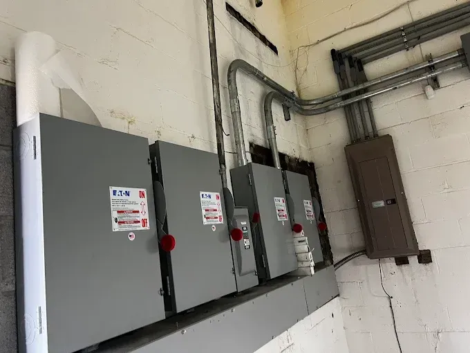 Electrical boxes mounted on a concrete wall. Gray metal boxes with red switches and wiring conduits.