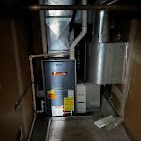 Furnace in a narrow enclosure, showing metal ducts, pipes, and control panel.