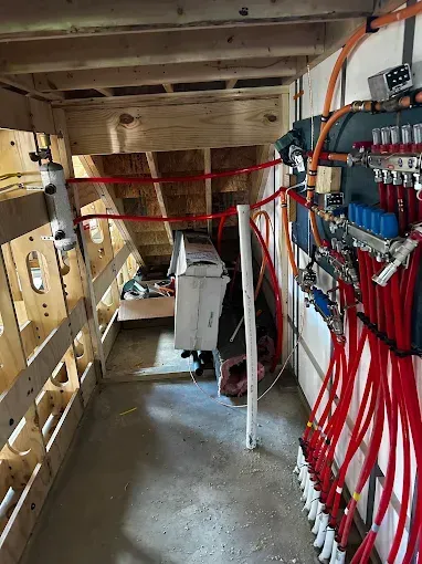 Plumbing and radiant heat system in a crawl space. Red pipes, blue manifolds, wooden framing, and a white PVC pipe.