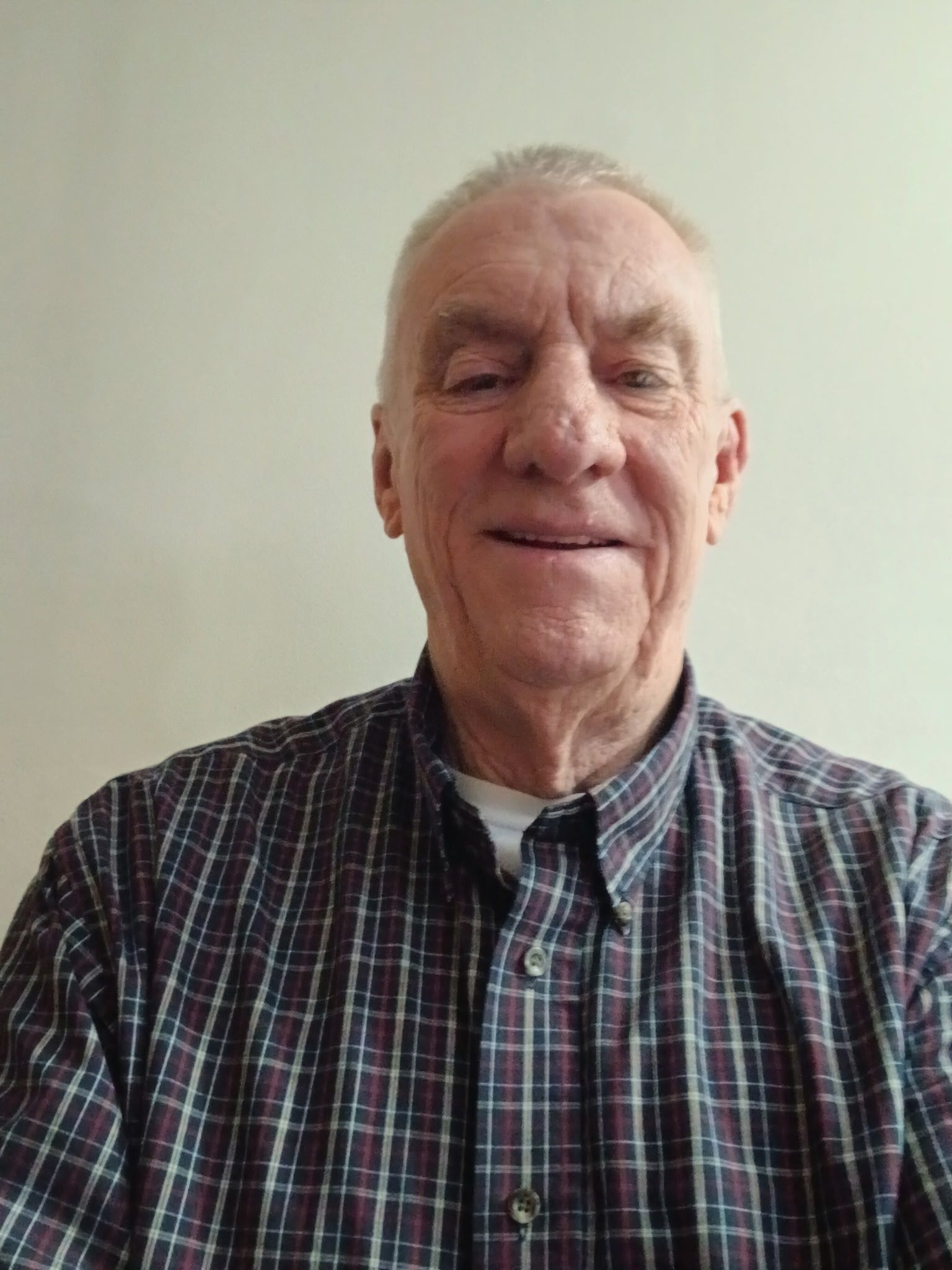 Man in a dark suit smiles, wearing a tie; light complexion, short gray hair.