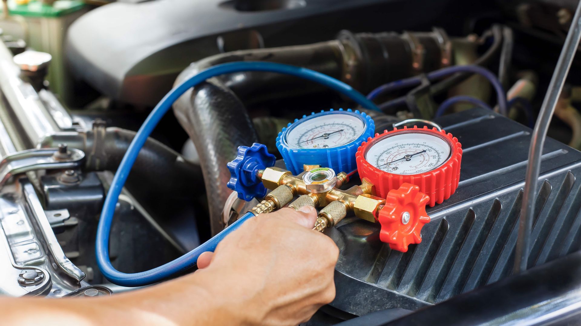 A person connecting gauges to a car engine, checking air conditioning system.