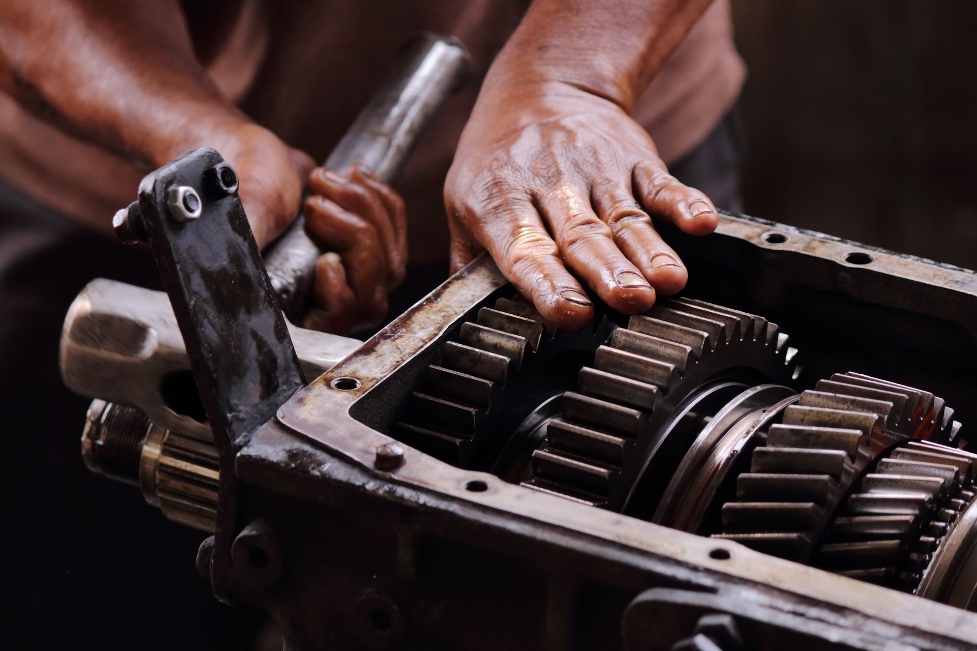 Mechanic working on gears inside a metal machine casing, hands covered in oil, using a tool.