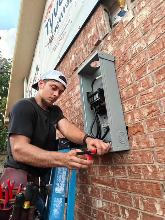 A man is working on an electrical box on a brick wall.