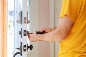 A locksmith repairing a door lock with a screwdriver. A locksmith repairing a door lock with a screwdriver.