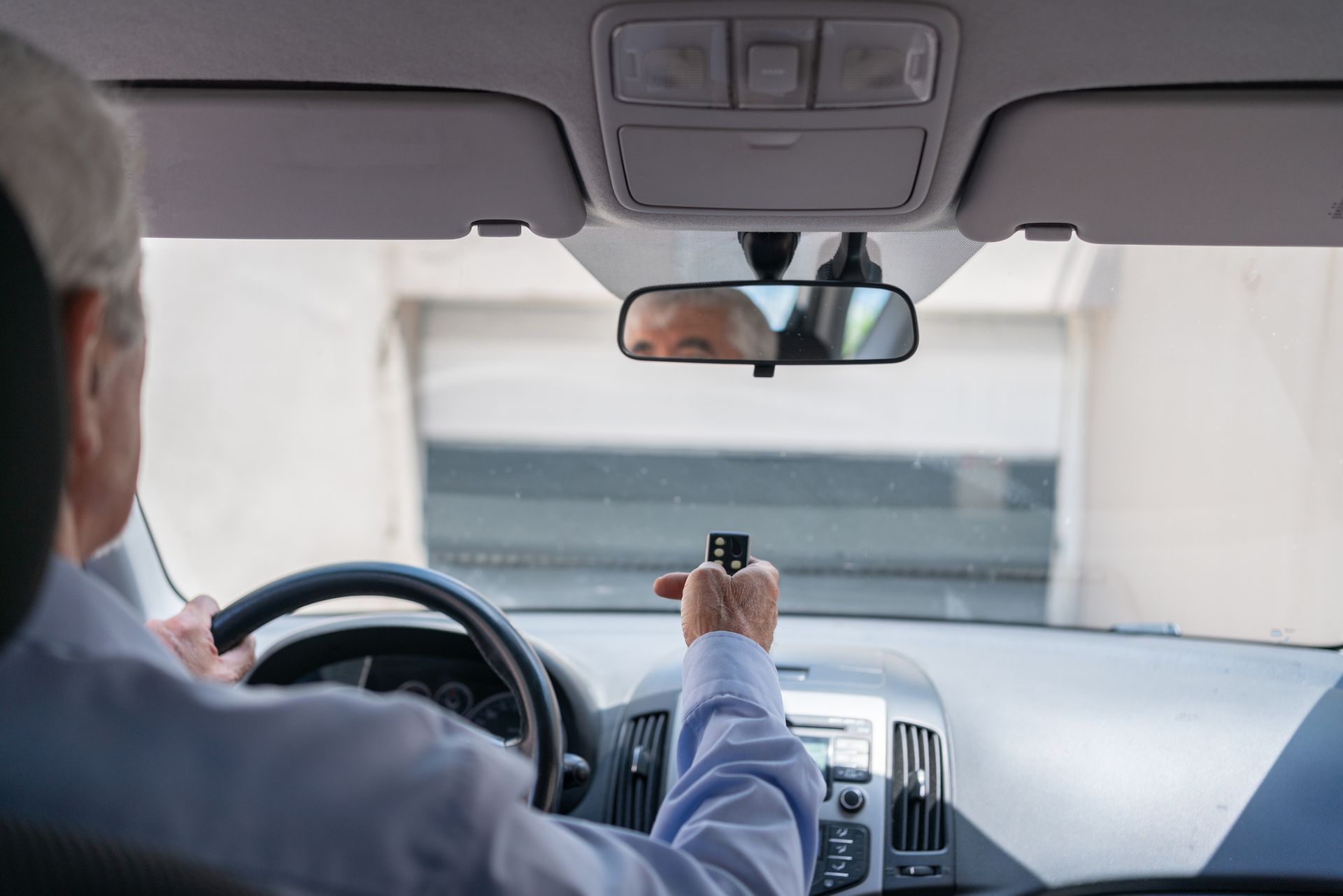 View of a man inside his vehicle using a garage remote to open the garage door. View of a man inside his vehicle using a garage remote to open the garage door.