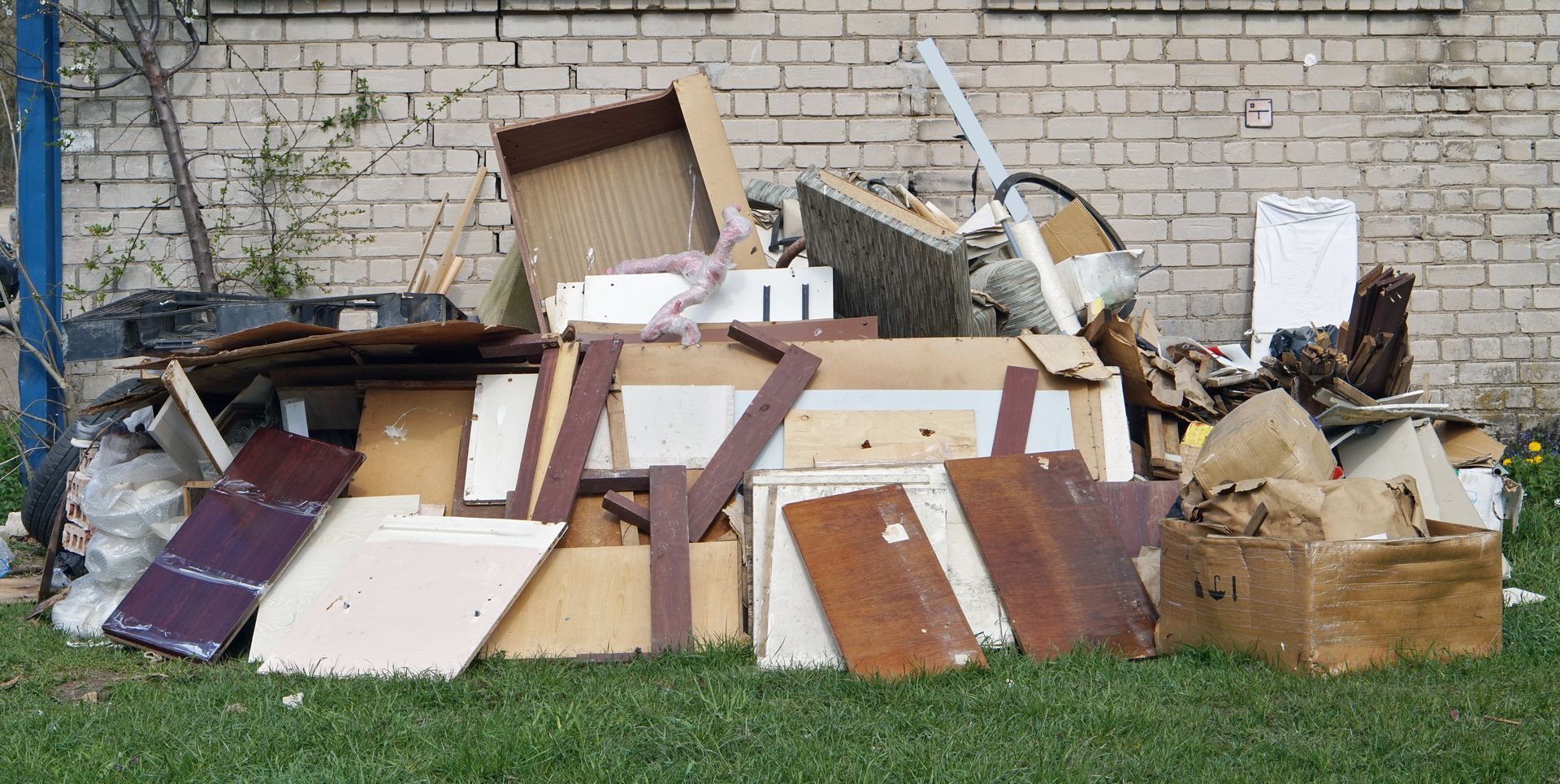 A pile of trash is sitting in the grass in front of a brick wall.