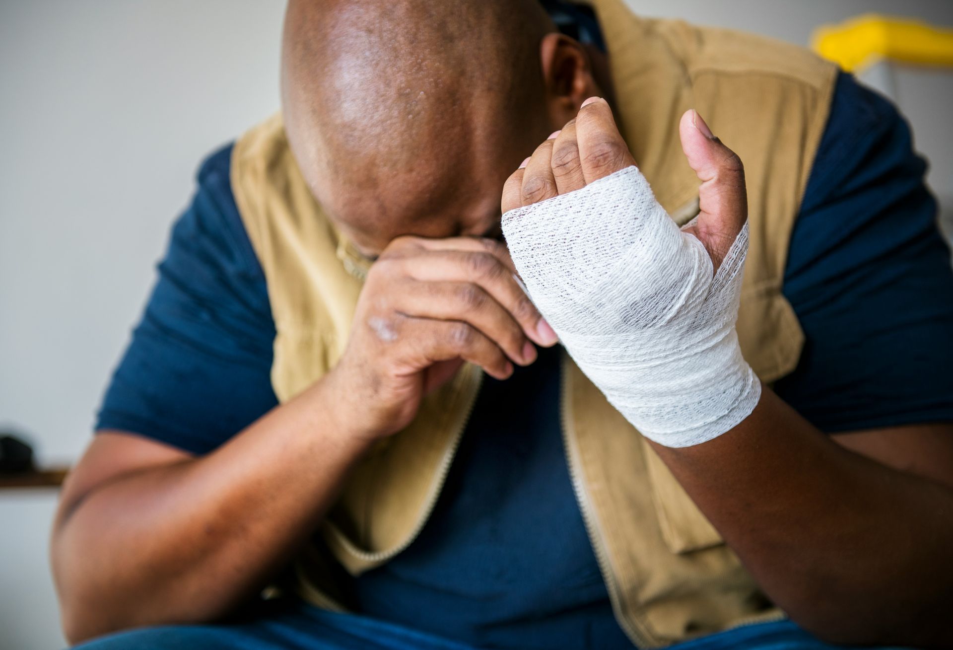 A man with a bandaged hand is covering his face with his hands.