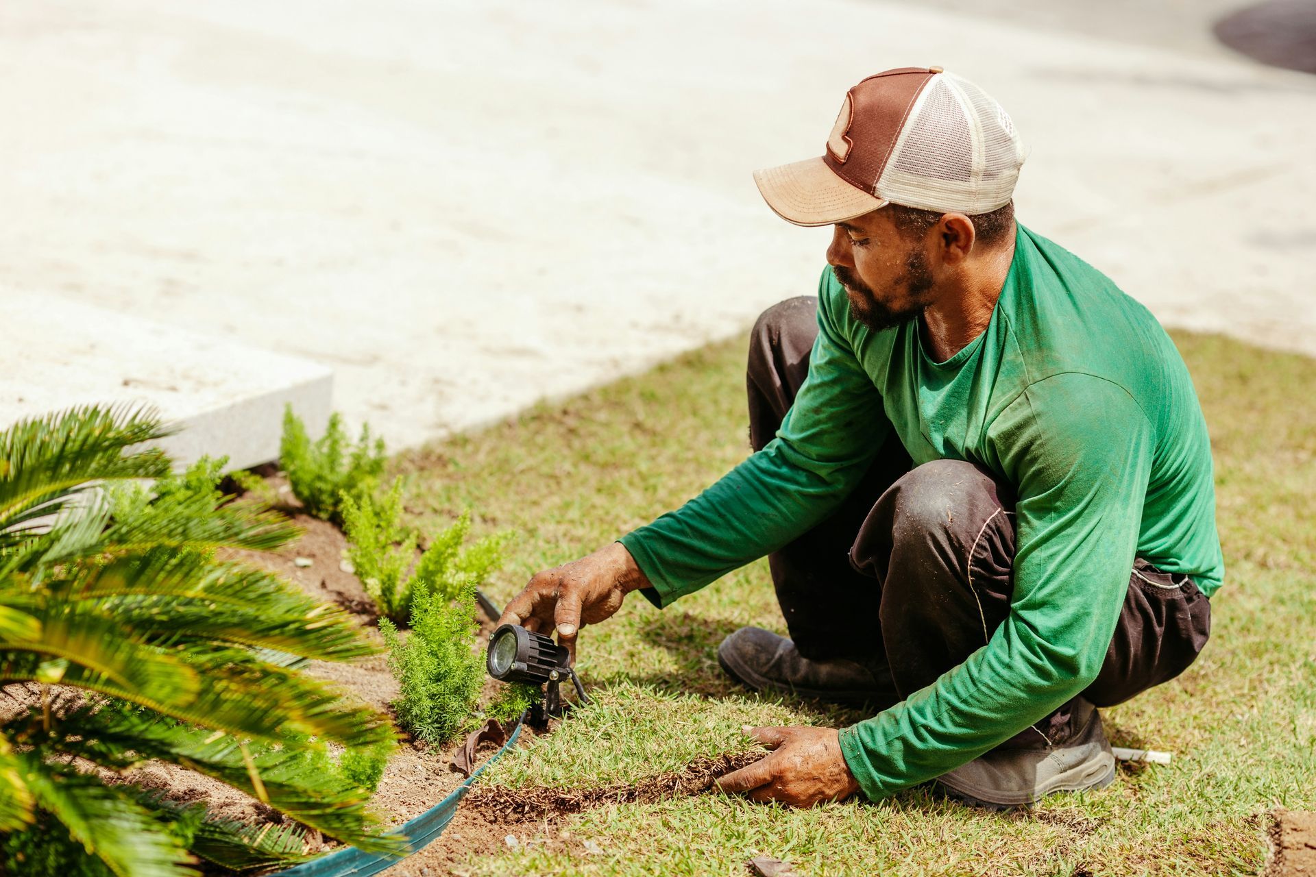 A man is kneeling down in a garden and watering plants.